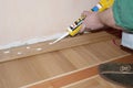 Repairman installing skirting board oak wooden floor with caulking gun silicone from cartridge. Flooring with wooden batten repair Royalty Free Stock Photo