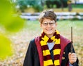 Boy in glasses stands in autumn park with gold leaves, holds book in his hands