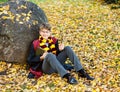 Boy in glasses stands in autumn park with gold leaves, holds book in his hands