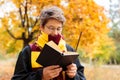 Cute pretty boy in costume of Harry Potter and scarf plays as a magician, reads book in autumn