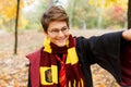 Cute pretty boy in costume of Harry Potter and scarf plays as a magician, reads book in autumn