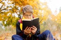 Cute pretty boy in costume of Harry Potter and scarf plays as a magician, reads book in autumn