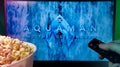 Person watching Aquaman and the Lost Kingdom movie on TV with popcorn and remote control. Stock editorial photo.