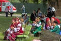 Performers in national costumes and other spectators watch a play during a free open festival.