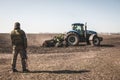 Kyiv, Ukraine - 03/23/2022: Ukrainian soldier of territorial defense looks at the tractor plowing the field Royalty Free Stock Photo