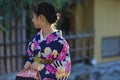 KYOTO, JAPAN - NOVEMBER, 8, 2019: Beautiful Japanese Geisha Girl Posing in Floral Silk Kimono in Traditional Environment in Kyoto