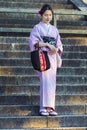 KYOTO, JAPAN - NOVEMBER, 8, 2019: Shy and Beautiful and Serene Japanese Lady Posing in Geisha Kimono On Shrine Stairway in Kyoto