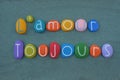 L`amour toujours, french phrase meaning Love always composed with handmade multicolored stone letters over green sand