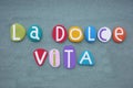 La dolce vita, italian lifestyle slogan composed with multi colored stone letters over green sand