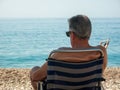 Old man with extra fat and excess skin sitted on a beach chair looking at the sea