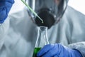 Lab technician holding dropper with dripping in flask. Scientist in personal protective equipment suit are working and analyzed