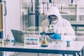 Lab Technician in Personal protective equipment PPE suit looking into microscopes glass windows on foreground