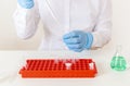 A lab worker in blue medical gloves sits at a workplace and pours liquid into a small test tube