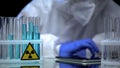 Lab worker in gloves testing blue radioactive liquid in test tube, notes on tab Royalty Free Stock Photo