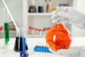 Lab worker holding flask with orange liquid near table Royalty Free Stock Photo