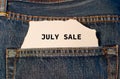 Label with text july sale in the pocket of blue denim jeans.