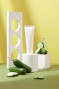 Labelless cosmetic tube is displayed on a minimalist background with some decorative props and fresh cucumbers. Cosmetics with