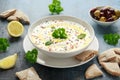Labneh cream cheese dip with olive oil, salt, herbs served with olives, pita bread in white bowl