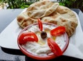 Labneh and tomatoes in a red bowl, next to pita flat bread. Arab food on a table