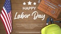 A poster for the labor day with a yellow hard hat on a wooden table.