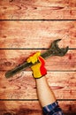 Men`s heavy hand in yellow gloves is holding a large old iron key on wooden background