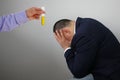 Laboratory assistantÃ¢â¬â¢s hand holds a test tube with yellow liquid, businessman sits with his head in his hands, symbol of