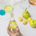 The lab assistent hand holds a flask of nitric acid on the background of the fruit lying on the table Royalty Free Stock Photo