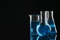 Laboratory glassware with blue liquids on black background