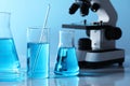 Different laboratory glassware with light blue liquid and microscope on table Royalty Free Stock Photo