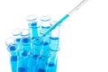 Laboratory pipette with drop of blue liquid over test tubes for an experiment in a science research laboratory on white Royalty Free Stock Photo