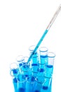 Laboratory pipette with drop of blue liquid over test tubes for an experiment in a science research laboratory on white Royalty Free Stock Photo