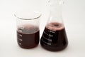 A laboratory set of glassware of conical and volumetric flasks that contains dark red liquid fluid with bubbles after a scientific