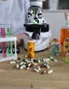 Laboratory setup with microscope, test tubes, and scattered pills on a wooden table in a science Royalty Free Stock Photo