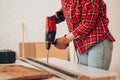 Laborer girl drilling plank with drill on the table