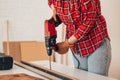 Laborer girl drilling plank with drill on the table