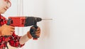 Laborer girl in protective gloves drills concrete wall with drill