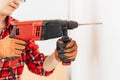 Laborer girl in red shirt drills concrete wall with drill