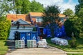 Laborers replacing a roof on a house with a blue dumpster and supplies in the driveway