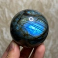 Labradorite sphere with a vivid blue labradorescence held between fingers. This Royalty Free Stock Photo