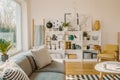 Ladder with blanket standing next to white wooden rack with decor, books and plants in bright living room interior with grey