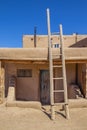 Ladder leading to second story apartments on traditional mud adobe pueblo with porch and old grunge wooden door in American Royalty Free Stock Photo