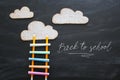 Ladder made of colorful chalks and pencils next to clouds over blackboard background.