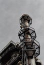 Ladders and expanded metal walkways around a smokestack, urban industrial steel mill