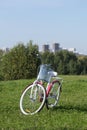 Ladies` bike in red and white. Stands in the park on the lawn. Multi-storey buildings under construction are visible on the