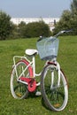 Ladies` bike in red and white. Stands in the park on the lawn. Multi-storey buildings under construction are visible on the