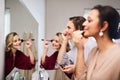 The ladies wanna look as pretty as can be. a group of beautiful young bridesmaids applying make-up in front of a mirror