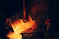 Ladle container with liquid molten metal and worker in protective helmet and face mask, industrial metallurgical factory