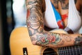 lady with arm tattoos strumming acoustic guitar