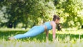 Lady athlete practices yoga pose Cobra and stretches back on green park meadow trees shadow
