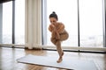 Lady balancing on one leg and keeping hands in namaste gesture at training room. Royalty Free Stock Photo